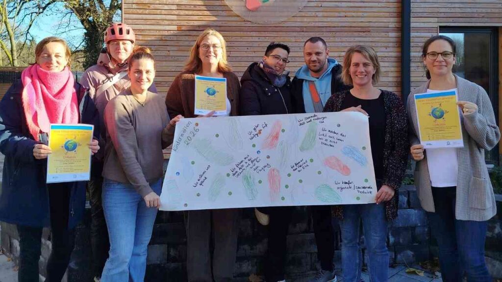 Gruppe von Personen hält ein großes Plakat mit bunten Zeichnungen und Texten in den Händen.