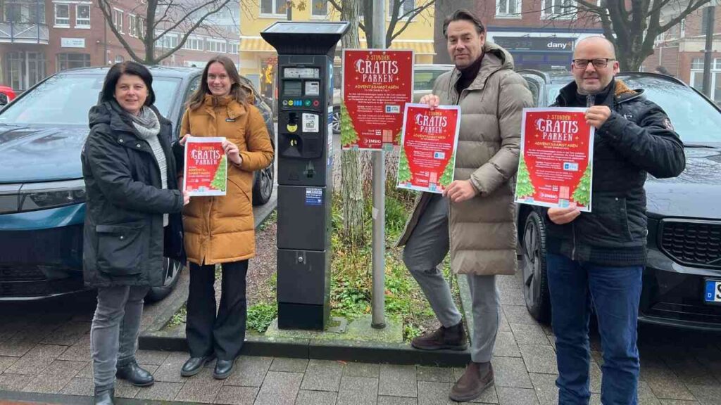 Vier Personen stehen neben einem Parkautomaten und halten Plakate mit der Aufschrift 'Kostenfreies Parken' während der Adventssamstage in Emsdetten.
