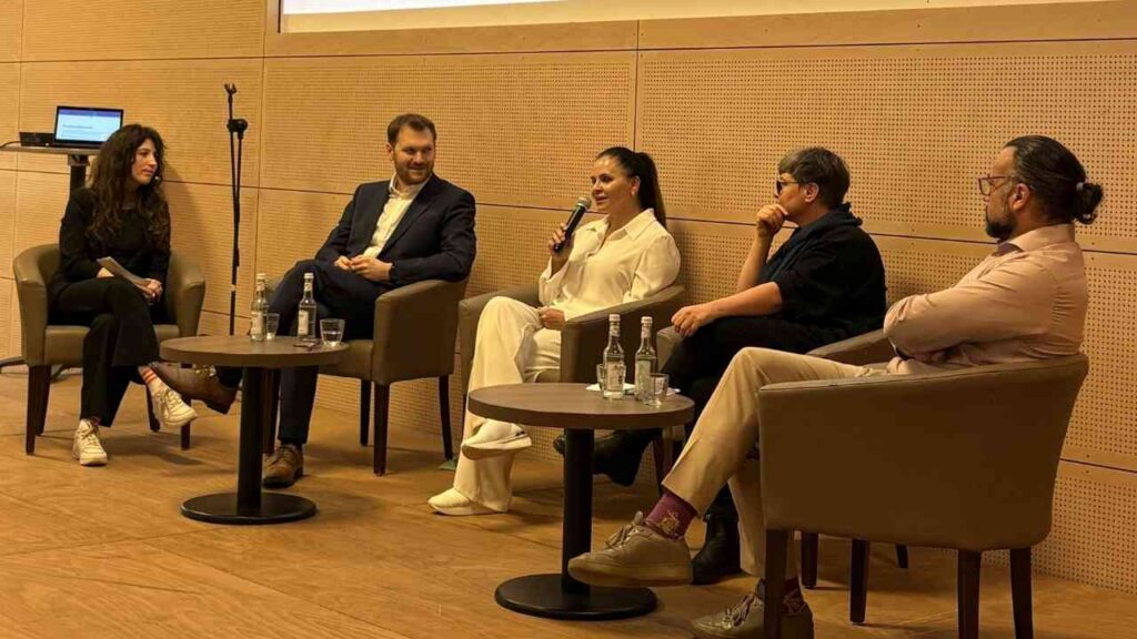 Podiumsdiskussion mit fünf Personen, die in einem modernen Raum sitzen und miteinander sprechen.