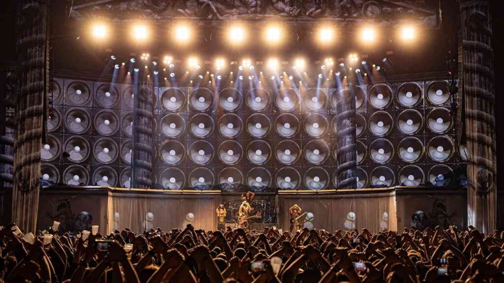 Live-Auftritt einer Band auf einer Bühne mit großen Lautsprechern und einer Menschenmenge vor ihnen.