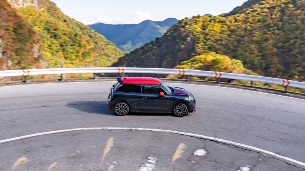 MINI John Cooper Works fährt auf einer kurvenreichen Straße in einer bergigen Landschaft mit herbstlichen Farben.