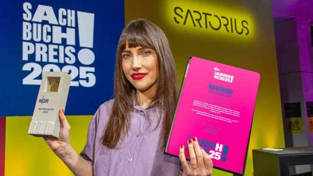 Frau hält den NDR Sachbuchpreis 2025 und eine Urkunde in der Hand, mit einem bunten Hintergrund.