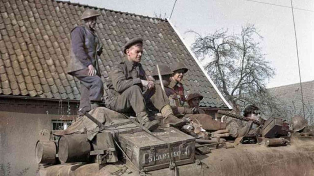 Soldaten in historischen Uniformen sitzen auf einem Panzer, umgeben von militärischer Ausrüstung.