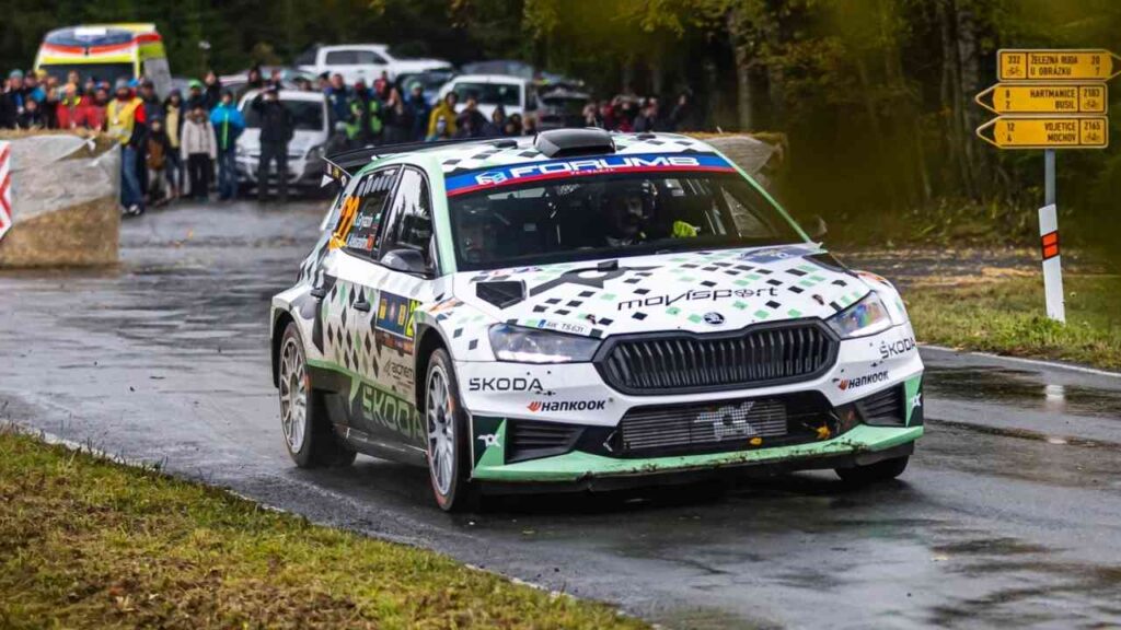 Rallyeauto von Škoda, das auf einer nassen Straße während eines Rennens fährt, mit Zuschauern im Hintergrund.