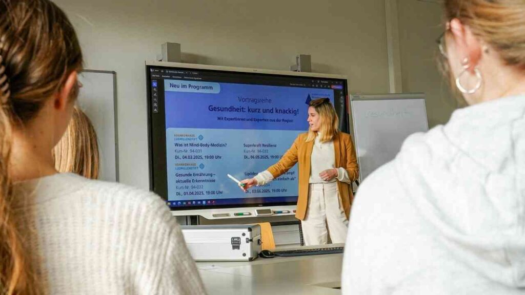 Frau präsentiert Gesundheitsvorträge an einer digitalen Tafel in einem Klassenraum.