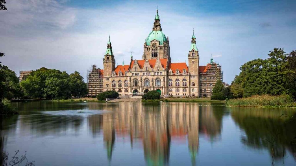Rathaus Niedersachsen mit grüner Kuppel und reflektierendem Wasser im Vordergrund.