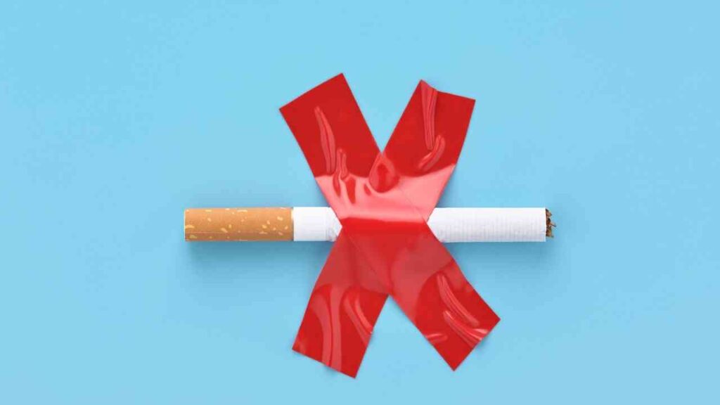Zigarette mit rotem Kreuz und Klebeband auf blauem Hintergrund, symbolisiert Rauchverbot.