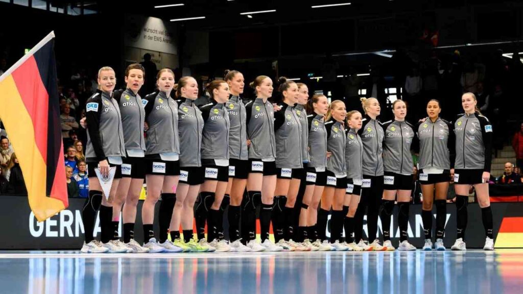 Deutsche Handballnationalmannschaft der Frauen in grauen Trikots, aufgestellt mit der Flagge im Hintergrund.
