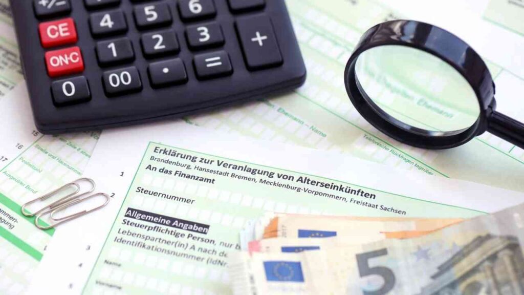 Schwarzer Taschenrechner, Lupe und Euro-Banknoten auf Steuerformularen zur Altersversorgung.