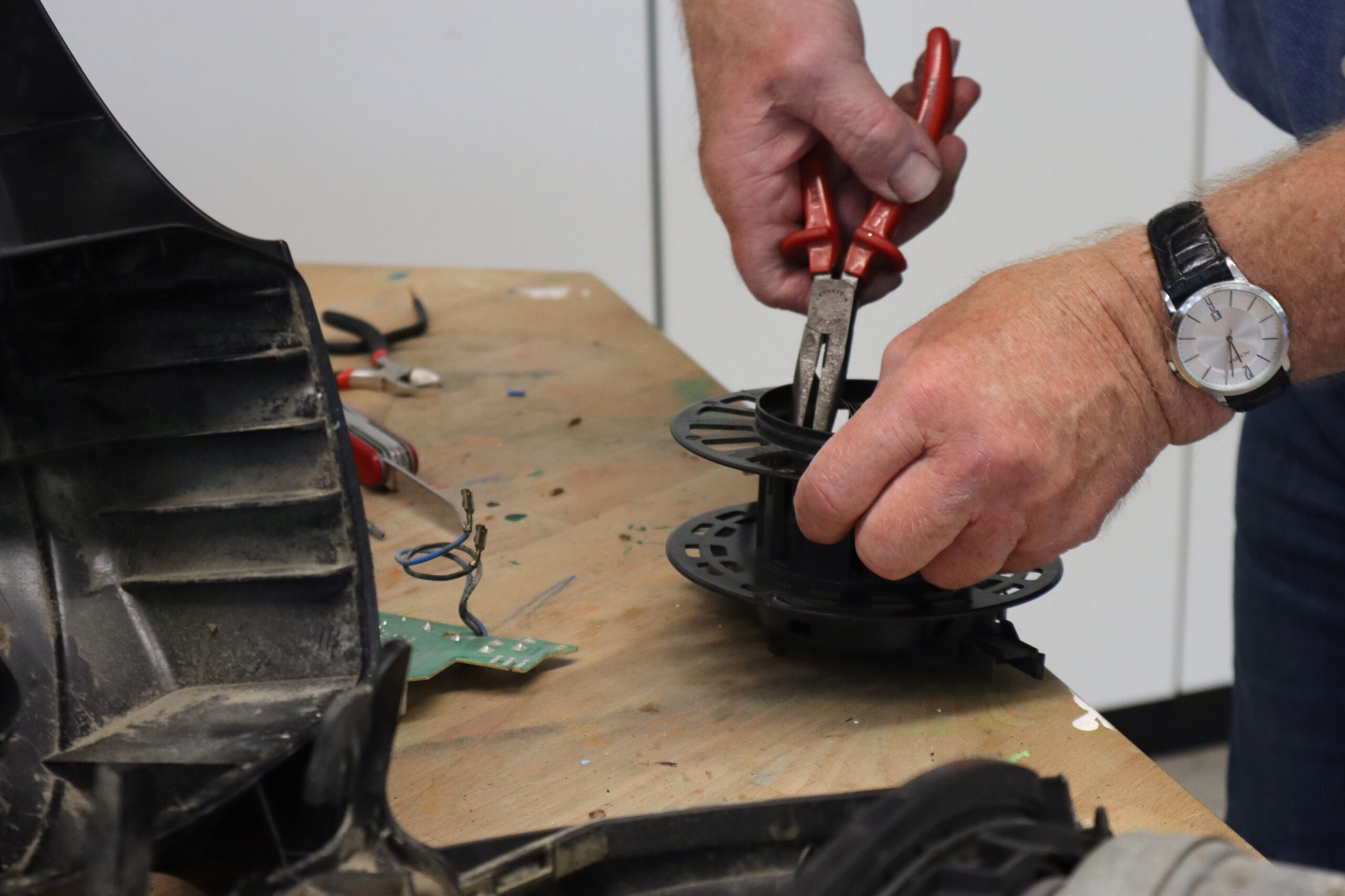 Hände eines Technikers, die mit einer Zange an einem mechanischen Bauteil arbeiten.