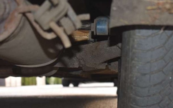 Unterseite eines Fahrzeugs mit sichtbarem Auspuffsystem und Reifenprofil.