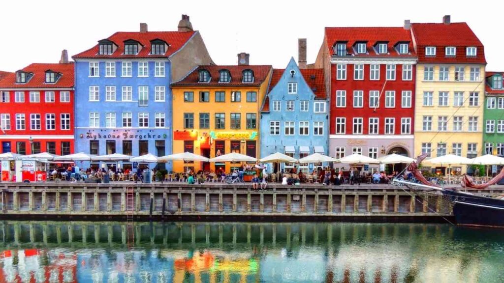 Bunte Gebäude am Wasser in Kopenhagen mit Cafés und Tischen im Freien.