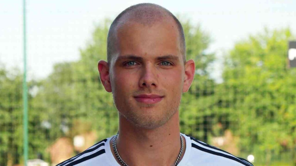 Porträt eines Mannes mit kurzem, glattem Haar, der ein sportliches Oberteil trägt und in die Kamera schaut.