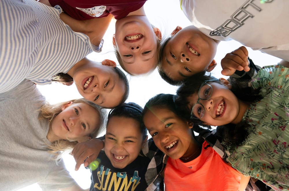 Gruppe von acht lächelnden Kindern, die in einem Kreis stehen und in die Kamera schauen.