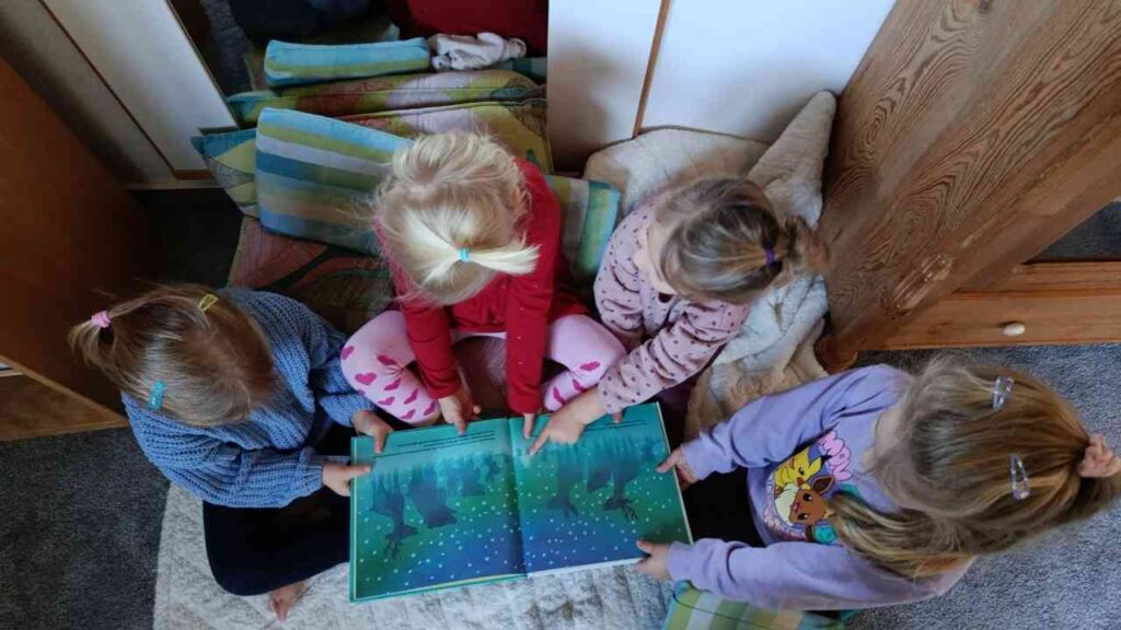 Vier Kinder sitzen auf einer Decke und schauen gemeinsam in ein Bilderbuch mit bunten Illustrationen.