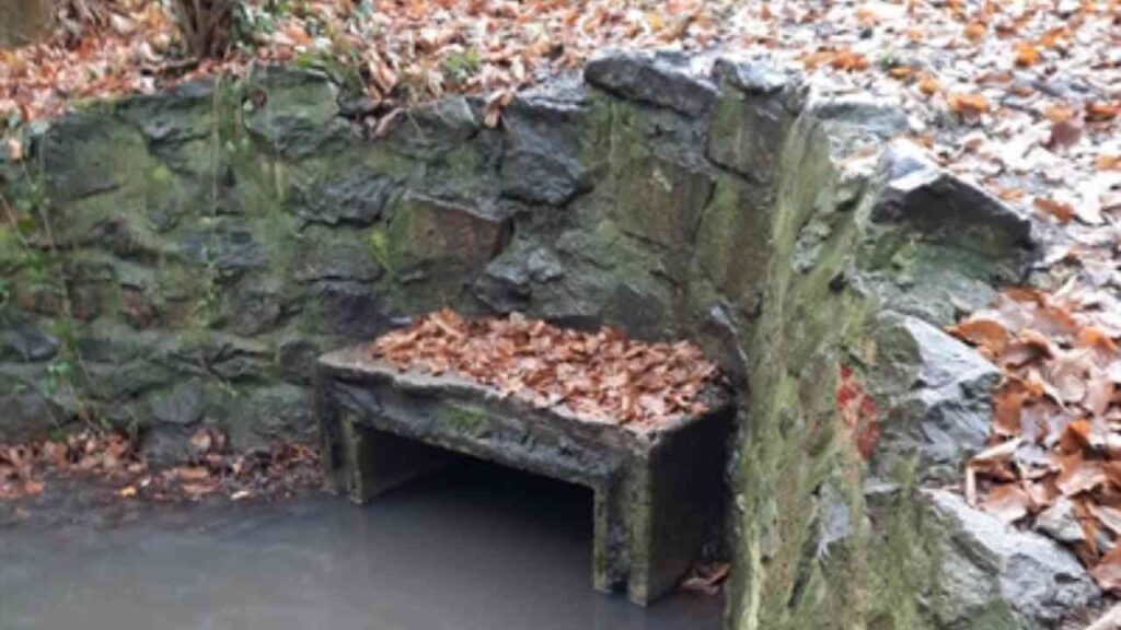 Steinerne Bank mit Laub in einem kleinen Wasserlauf in Gremmendorf.