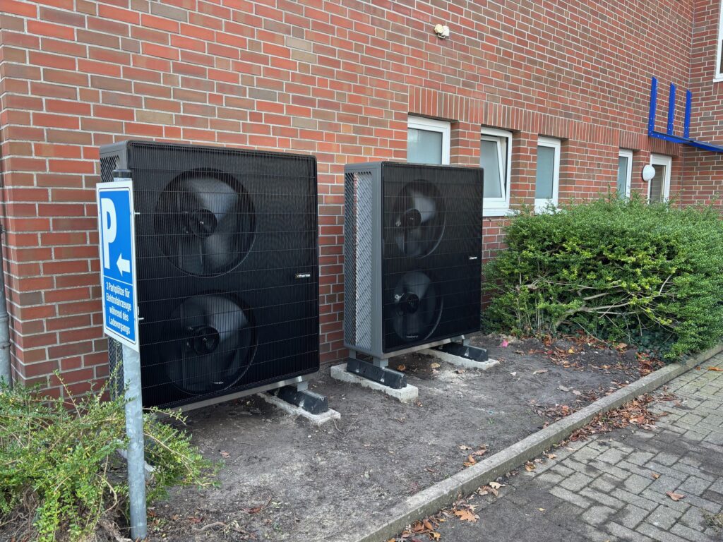 Zwei große Wärmepumpen mit Ventilatoren, auf einem gepflasterten Bereich neben einem Gebäude aufgestellt.