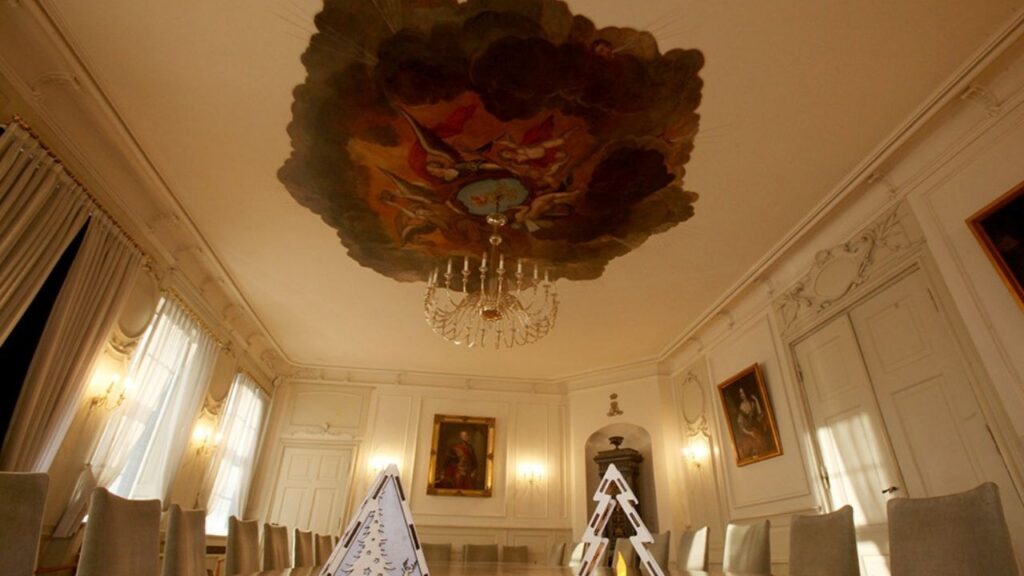 Weißer Saal im historischen Dienstgebäude des LBEG mit einem kunstvollen Deckenfresko und eleganten Möbeln.