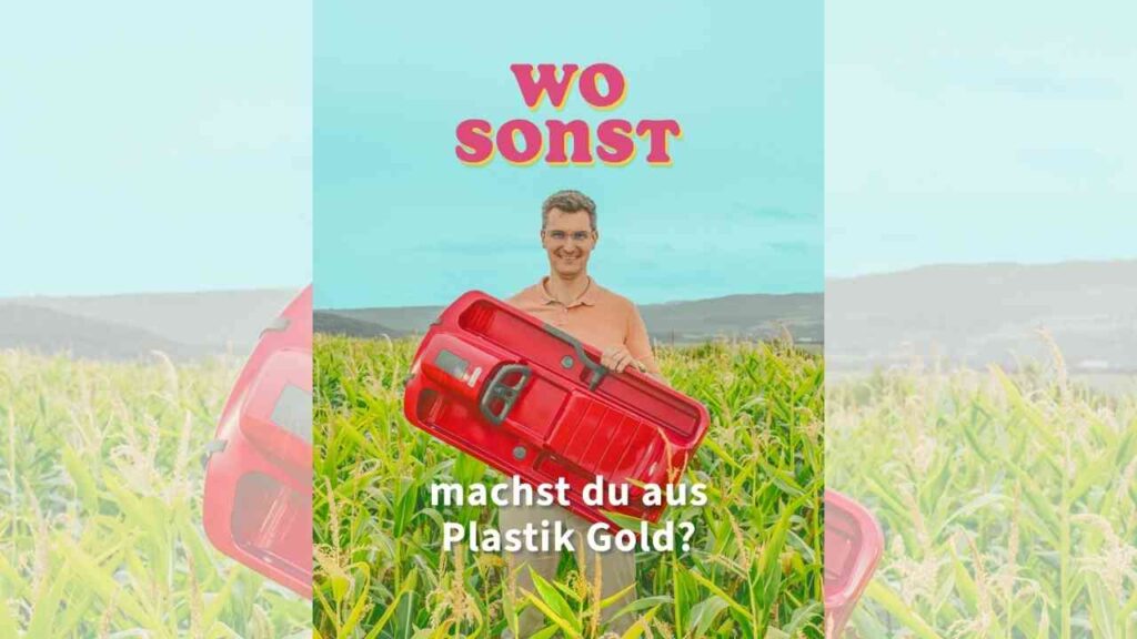 Mann hält ein rotes Spielzeugauto in einem Feld mit Maispflanzen, umgeben von blauem Himmel.