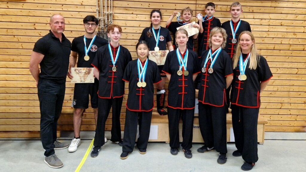 Gruppe von Kung-Fu-Schülern in Schwarz mit Medaillen und Trophäen nach einem Wettkampf.