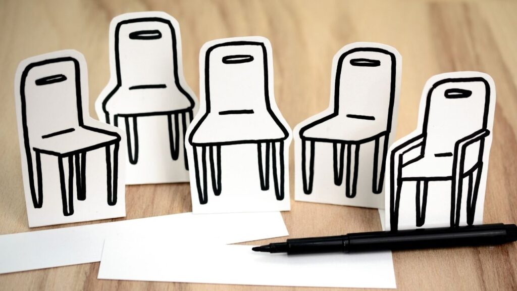 Fünf Pappstühle mit einfachen Zeichnungen und einem schwarzen Stift auf einem Tisch.