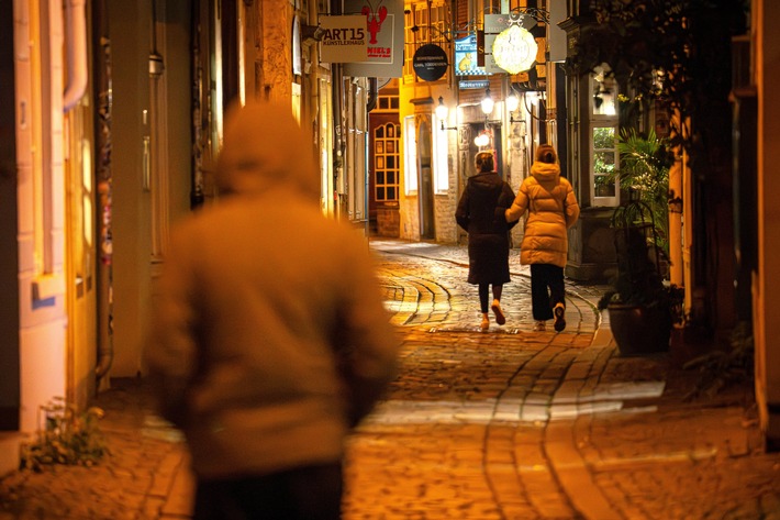 Zwei Personen in Winterkleidung, die eine schmale, beleuchtete Gasse in der Stadt entlanggehen.