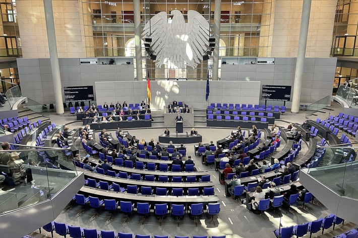 Plenarsaal des Deutschen Bundestages mit Abgeordneten in blauen Stühlen während einer Sitzung.