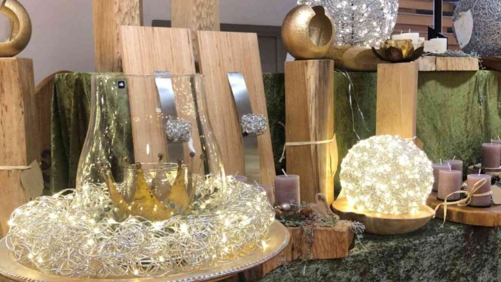 Dekorative Tischarrangements mit Lichtern, Kerzen und Glasobjekten auf einem Holzuntergrund.