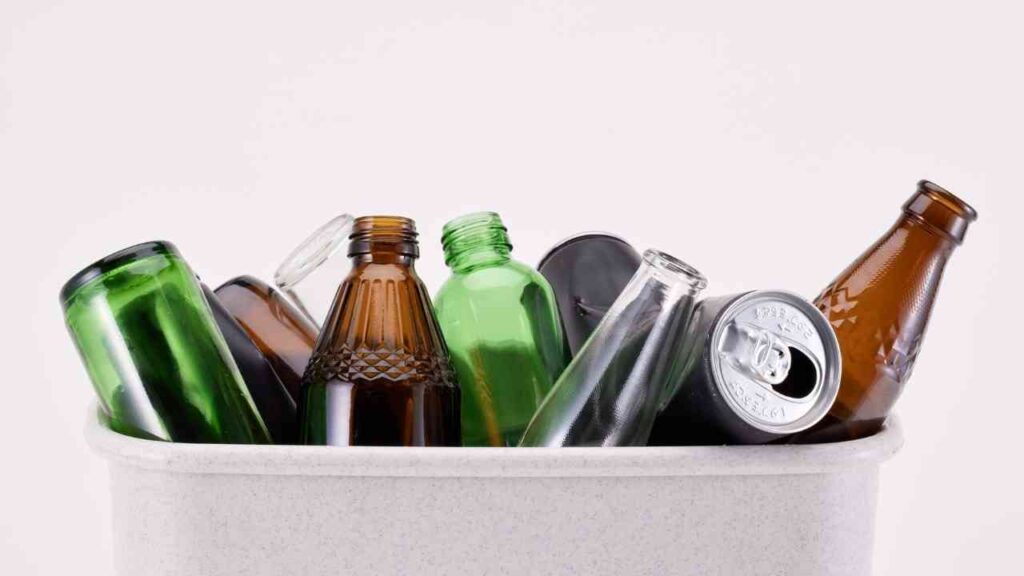 Verschiedene Glasflaschen in einem Behälter, darunter grüne, braune und klare Flaschen.