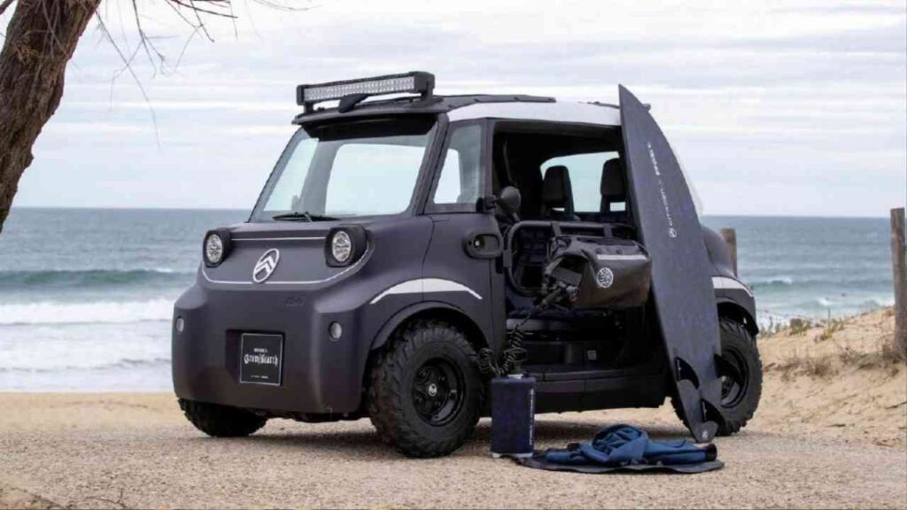 Kompakter Buggy mit Surfbrett und Ausrüstung am Strand, vor einer Küstenlandschaft.