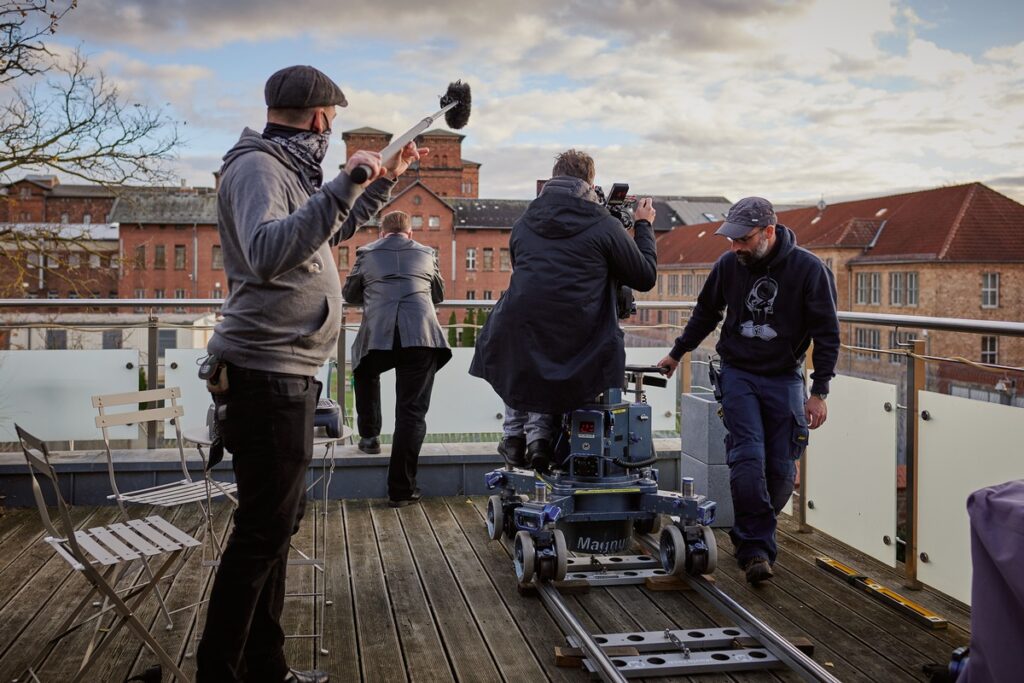 Filmcrew bei der Arbeit auf einer Terrasse mit Kamera und Schienen für die Aufnahme.