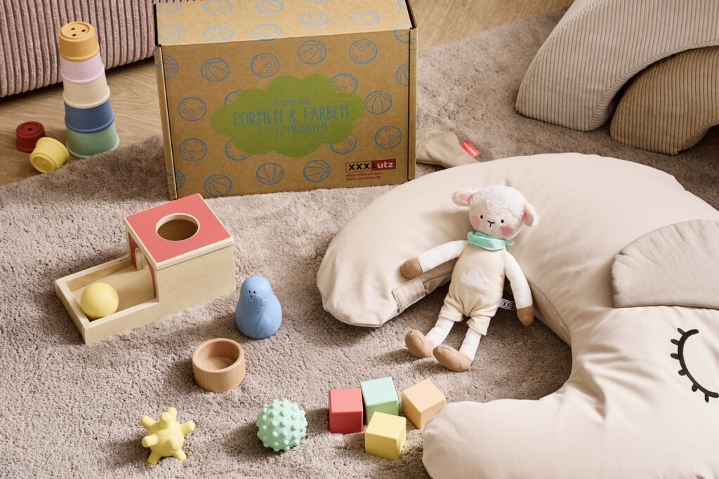 Bunte Spielzeuge und eine Babybox mit verschiedenen Spielzeugen auf einem Teppich in einem Innenraum.