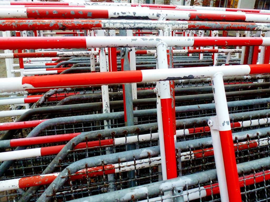 Rote und weiße Metallbarrieren, die in einem gestapelten Muster angeordnet sind, mit sichtbaren Abnutzungserscheinungen.