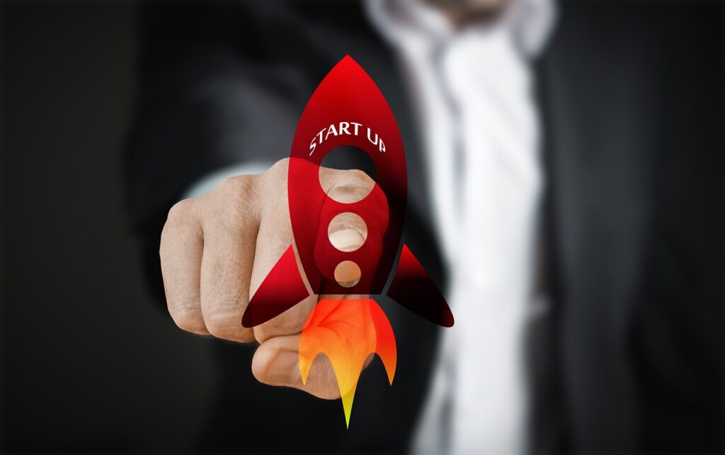 Rote Rakete mit der Aufschrift 'START UP', die von einer Hand gehalten wird, vor einem dunklen Hintergrund.
