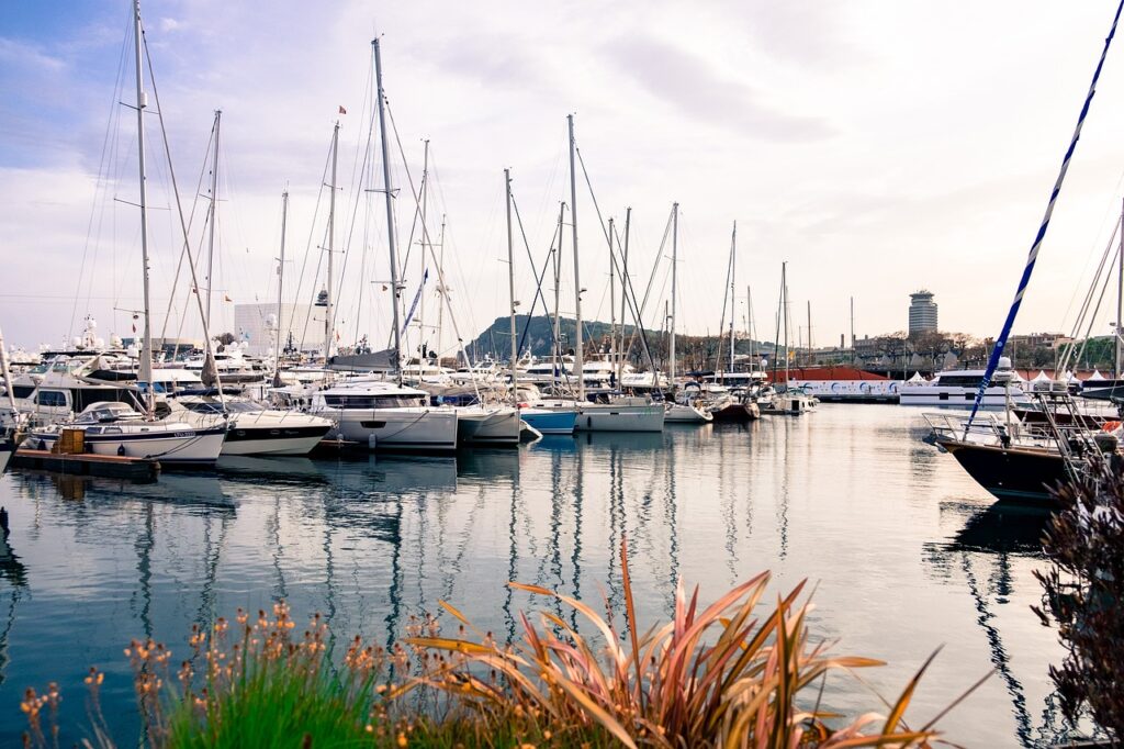 Mehrere Yachten und Boote im Hafen, reflektierend im Wasser mit einem sanften Himmel im Hintergrund.