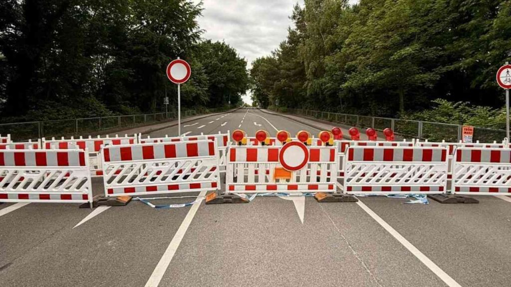 Bauabsperrung mit roten und weißen Absperrgittern auf einer Straße mit Verkehrszeichen.