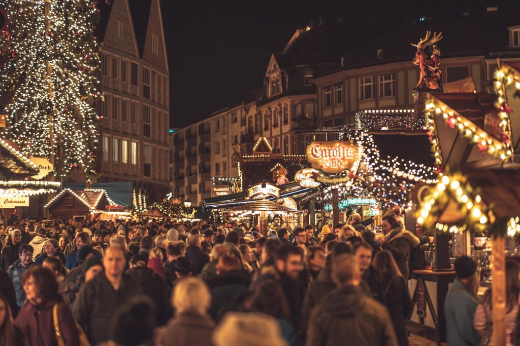 Belebter Weihnachtsmarkt mit festlicher Beleuchtung und vielen Besuchern in einer Stadt.