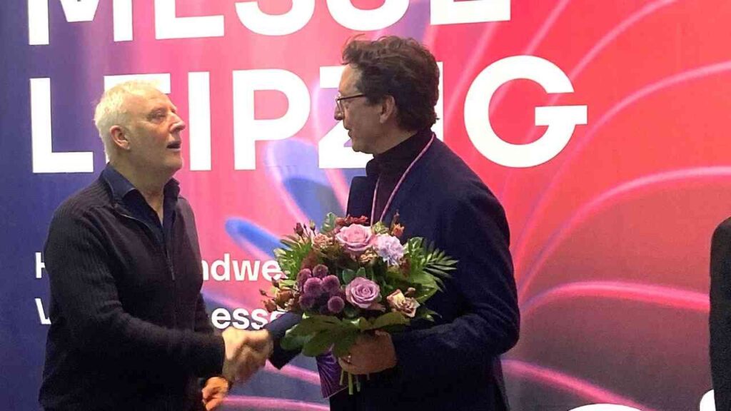 Zwei Männer schütteln sich die Hände während einer Preisverleihung auf der Messe Leipzig.