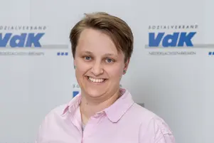 Porträt einer Person mit kurzen Haaren und einem lächelnden Gesicht, die ein helles Hemd trägt.