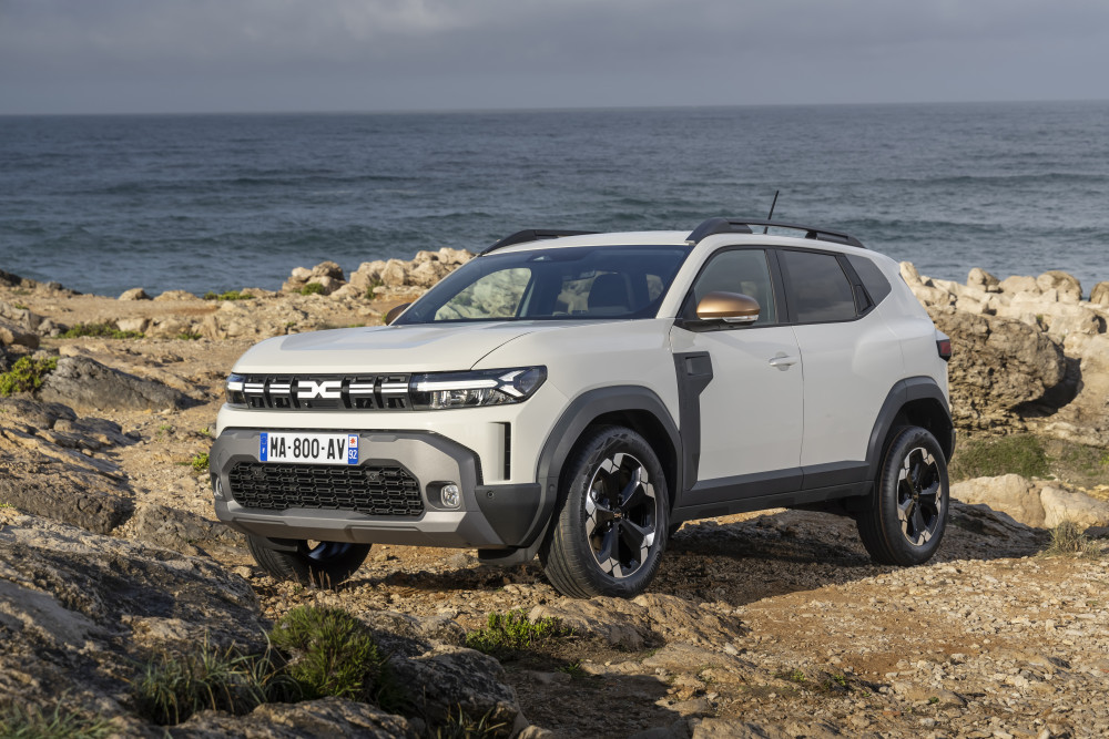 Dacia Bigster SUV in weißer Farbe, geparkt auf felsigem Terrain mit Meer im Hintergrund.