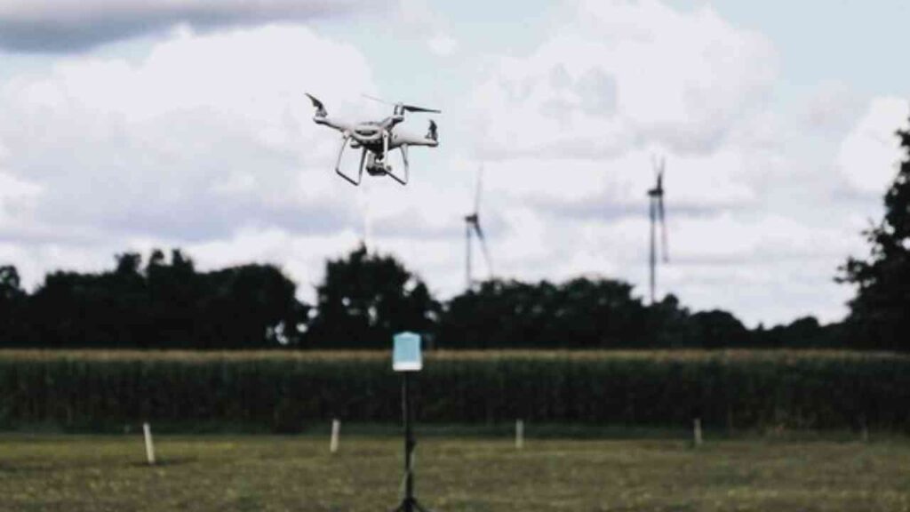 Ein Drohne schwebt über einem Feld mit Windkraftanlagen im Hintergrund.