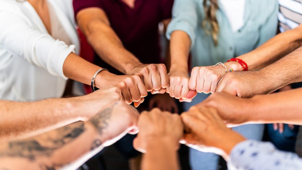Verschiedene Hände, die sich zum Fistbump treffen, symbolisieren Teamarbeit und Zusammenarbeit in einer Gruppe.