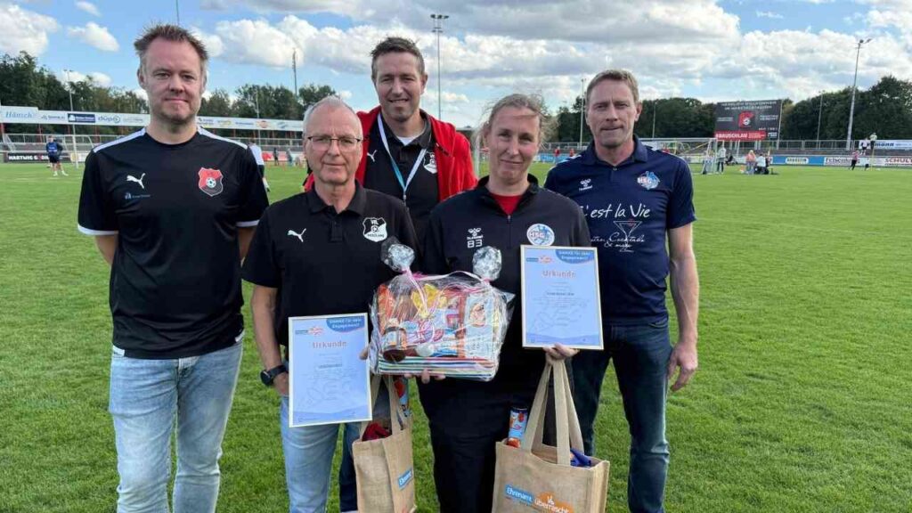 Fünf Männer stehen auf einem Fußballfeld, halten Urkunden und Geschenktüten in den Händen.