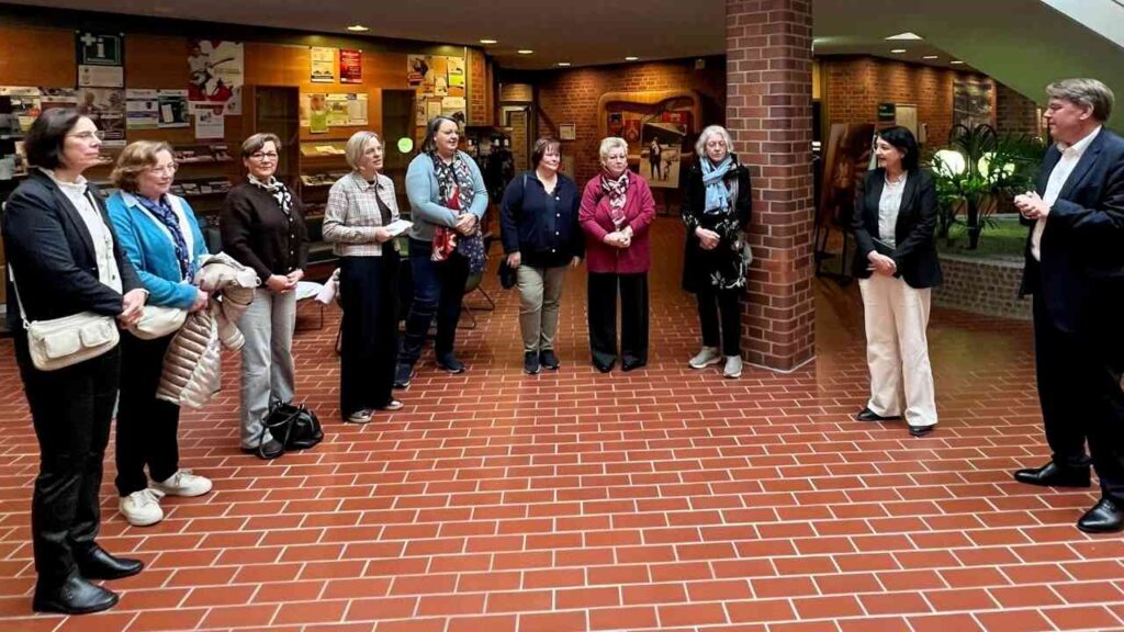 Gruppe von Frauen und Männern in einem Innenraum, die einem Redner aufmerksam zuhören.