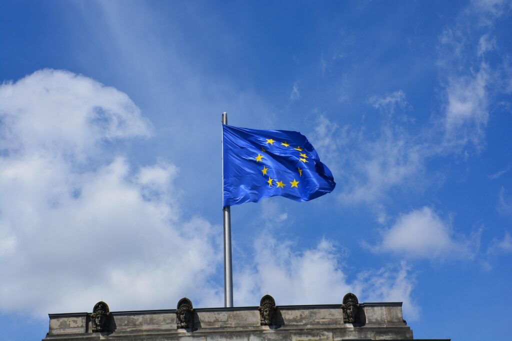 Europäische Flagge mit gelben Sternen auf blauem Hintergrund, weht im Wind vor einem klaren Himmel.