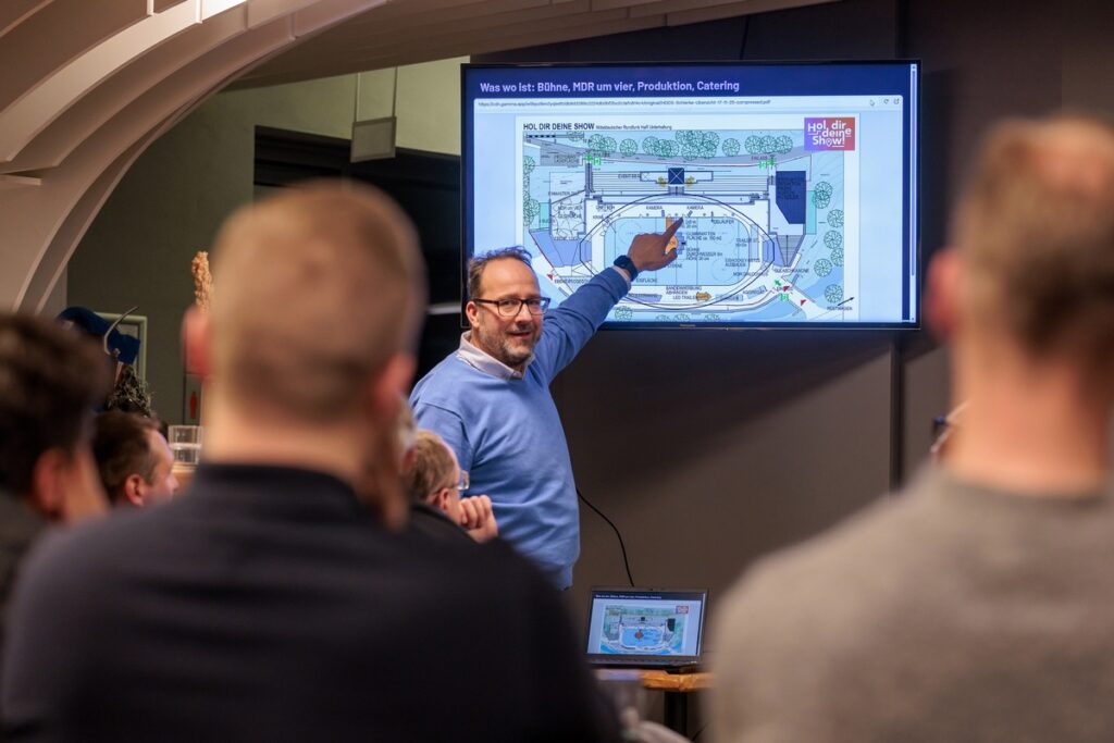 Mann zeigt auf einen Plan während einer Präsentation in einem modernen Veranstaltungsraum.