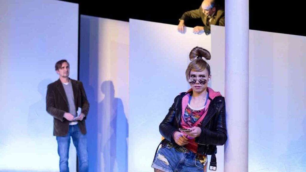 Schauspieler auf der Bühne eines Theaters mit einem weißen Hintergrund und einer Säule.