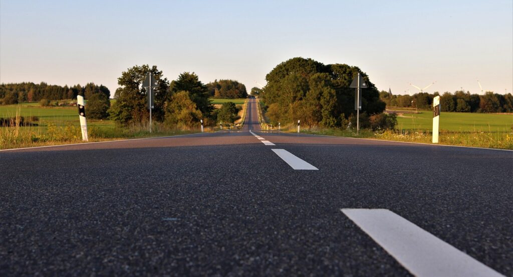 Blick auf eine asphaltierte Straße mit weißen Markierungen und Bäumen entlang der Strecke.