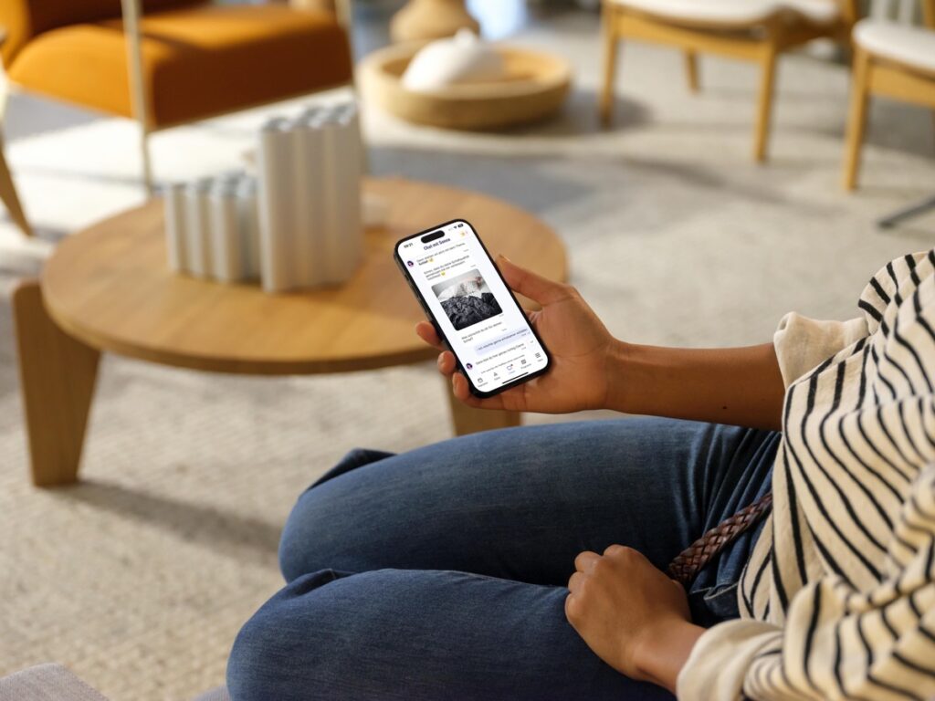 Person, die ein Smartphone in der Hand hält und auf den Bildschirm schaut, während sie auf einem Sofa sitzt.