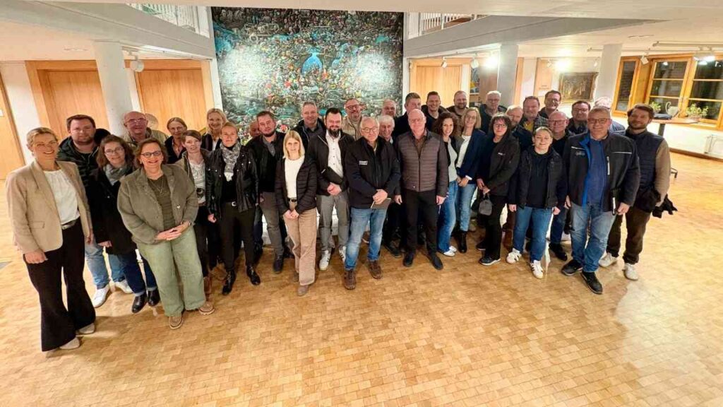 Gruppenfoto von Teilnehmern einer Veranstaltung in einem Innenraum mit Holzfußboden und Wandkunst.